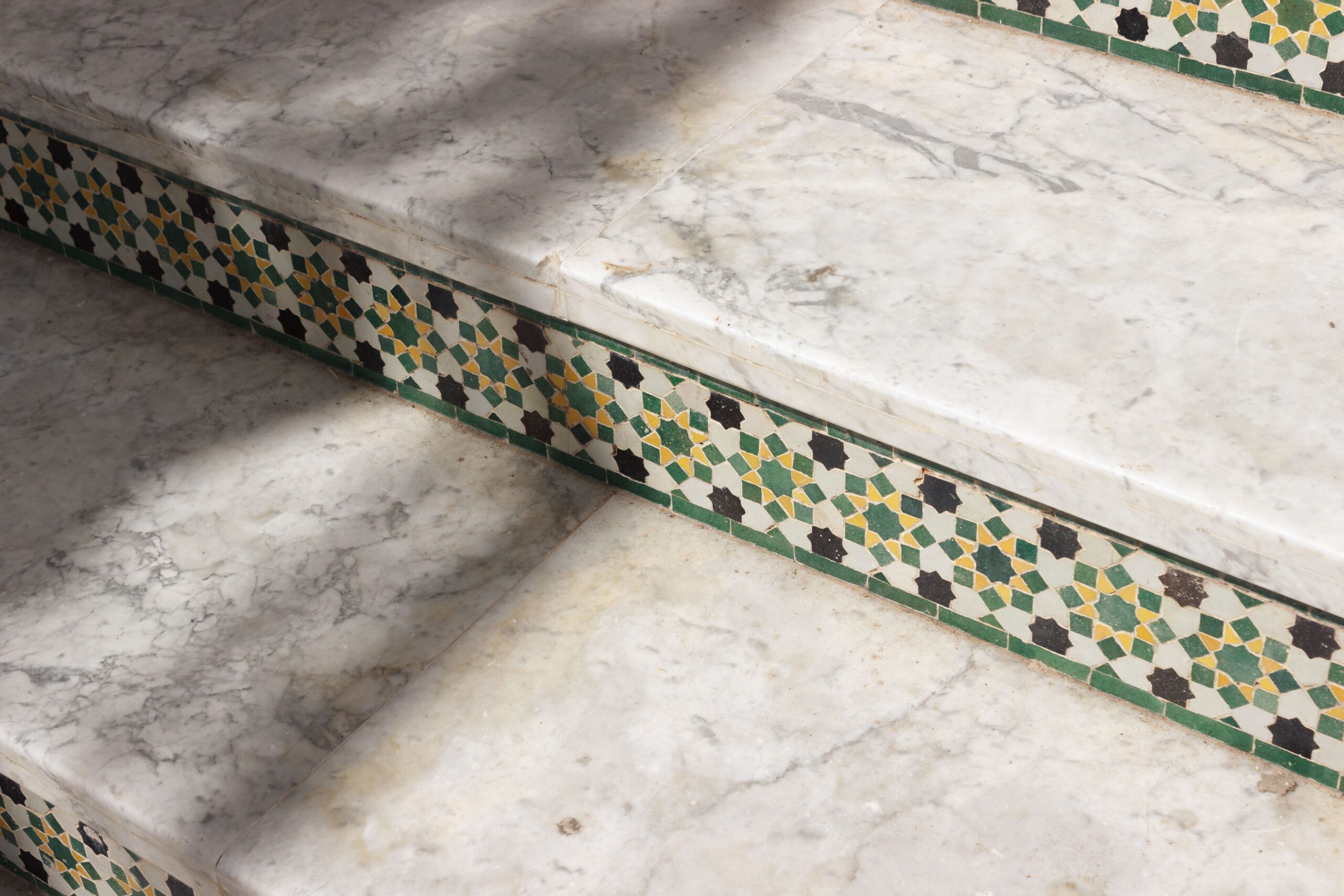 Detailed view of marble steps adorned with intricate mosaic tiles casting soft shadows.